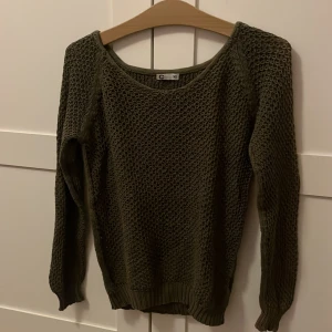 Olivgrön stickad tröja - Säljer en olivgrön stickad tröja. Tröjan har långa ärmar och en rund halsringning. Sliten och kanske lite missfärgad på sidan