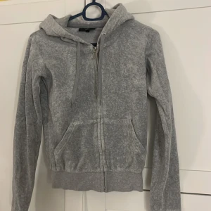 Grå hoodie från Juicy Couture - Säljer en grå hoodie från Juicy Couture. Knappt använd, men metal grejerna som ska sitta på snörena har åkt av. I strl xxs