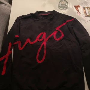 Svart långärmad tröja från Hugo - Snygg svart långärmad tröja från Hugo med röd logotyp i ett stort, stilrent tryck över bröstet. Perfekt för en trendig och avslappnad look. Storlek M men sitter som L, aldrig använd 