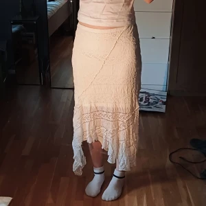 Långkjol från Bik Bok - Säljer en vacker beige långkjol från Bik Bok med volangdetaljer. Kjolen har en asymmetrisk nederkant och är tillverkad i ett lätt och luftigt material, perfekt för varmare dagar.