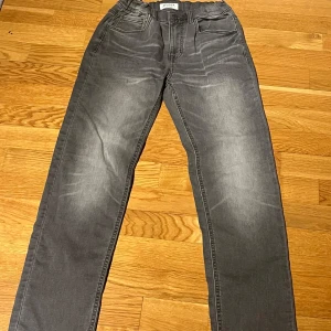 Grå byxor från Lindex - Säljer ett par grå byxor från Lindex i storlek EUR 158. Byxorna har en klassisk design med fickor både fram och bak samt en knapp i midjan. Perfekta för en stilren look.