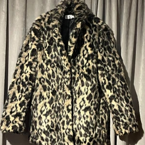 Leopardmönstrad pälsjacka 38 NA-KD - Säljer en trendig leopardmönstrad pälsjacka från NA-KD. Jackan har en klassisk design och är perfekt för att göra ett statement. Den är både varm och stilren, vilket gör den idealisk för kyligare dagar. Använd en gång!