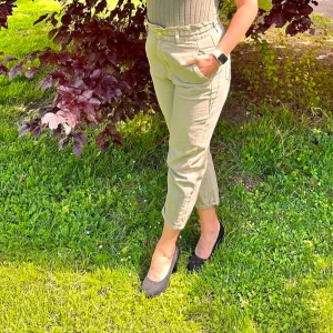 Militärgröna byxor med hög midja - Snygga militärgröna byxor med hög midja och normal passform. Perfekta för en avslappnad stil med fickor och knappdetaljer. Passar bra till både vardag och mer uppklädda tillfällen.