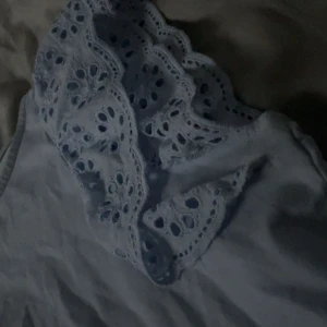 Ljus blå topp - Säljer en söt ljus blå topp från Lindex med vackra spetsdetaljer på ärmarna. Perfekt för en somrig look. Toppen är i barnstorlek 146/152 och har en luftig passform.