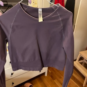Lila långärmad träningstopp från Index - Snygg lila långärmad topp från Index. Den är croppad med ribbade detaljer vid ärmslut och nederkant. Perfekt för en stilren och bekväm look.