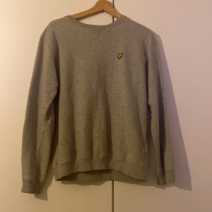 Grå tröja från Lyle & Scott - Säljer en stilren grå tröja från Lyle & Scott med deras ikoniska logga på bröstet. Tröjan har långa ärmar och en rund halsringning, perfekt för en avslappnad look, den är för 14-15 år i storlek men passar lika bra som s och är knappt använd.