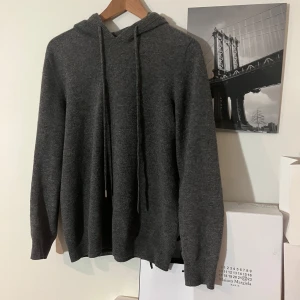 Grå hoodie i cashmere - Säljer en stilren grå hoodie med huva. Tröjan har långa ärmar och ribbade muddar vid ärmslut och nederkant. Tröjan är i 100% cashmere Perfekt till vintern eller efter ett skidåk⛷️Hör av er vid frågor så svarar vi så fort som möjligt!😁✅