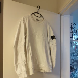 Vit sweatshirt från Stone Island - Säljer en stilren vit sweatshirt från Stone Island med broderad logga på bröstet och en ikonisk patch på ärmen. Tröjan har rund hals och långa ärmar, perfekt för en avslappnad look.