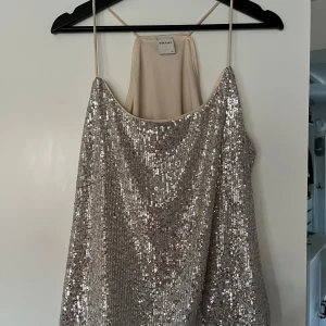 Glittrig linne från ONLY - Säljer ett glittrigt linne från ONLY i silver med tunna axelband. Perfekt för en festlig kväll eller nyårsfirande. Linnet har en lös passform och är täckt med paljetter som ger en glittrande effekt.