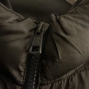 Svart dunjacka från Moncler - Snygg svart dunjacka från Moncler med dragkedja och hög krage. Jackan har ett quiltat mönster och Moncler-logga på ärmen. Perfekt för kyliga dagar.