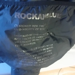 Svart dunjacka från Rockandblue - Snygg svart dunjacka från Rockandblue med hög krage och justerbar huva. Jackan har en stilren design med dragkedja och knappar framtill samt praktiska fickor med dragkedja. Perfekt för kalla dagar. Inköpt förra vintern och sparsamt använd nypris 3700