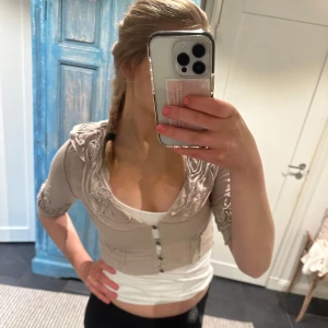 Beige bolerotopp med knappar - Säljer en beige bolerotopp med knappar framtill och trekvartsärmar. Toppen har en unik design med volangdetaljer vid axlarna. Perfekt för att lägga till en touch av stil till din outfit. Verkligen sä himla fin!🥰