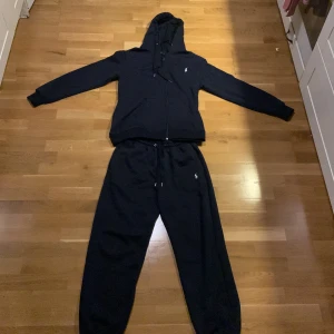 Mörkblå  hoodie och byxor från Ralph Lauren - Säljer en mörkblå hoodie och matchande byxor från Ralph Lauren. Hoodien har dragkedja och långa ärmar, med en liten broderad logga på bröstet. Byxorna har en elastisk midja och en broderad logga på benet. Perfekt för en avslappnad stil.