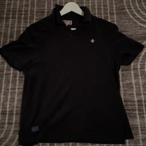 Svart kortärmad t-shirt från Morris - Tja!  Säljer en stilren svart t-shirt från Morris med en liten broderad detalj på bröstet. T-shirten har en klassisk krage och är kortärmad. Den är lite för bred för mig som är 174 63 kg. Skriv gärna om du har några frågor!