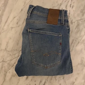 Replay Anbass - Snygga blå jeans från Replay med klassisk femficksdesign och knappgylf. De har en lätt tvättad look och en läderpatch med Replay-logga på baksidan. Perfekta för en avslappnad stil.