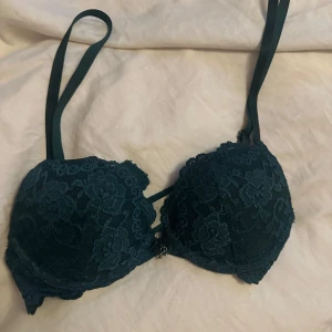 Mörkgrön spets-push up bh - Säljer en elegant mörkgrön bh med spetsdetaljer. Den har justerbara axelband och en vacker spetsdesign som ger en feminin touch. Perfekt för att känna sig extra fin under kläderna.