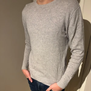 Grå stickad tröja - Säljer en stilren grå stickad tröja med rund halsringning. Tröjan har långa ärmar och ribbade muddar vid ärmslut och nederkant. Perfekt för kyligare dagar. 10% Kashmir 90% merinoull 