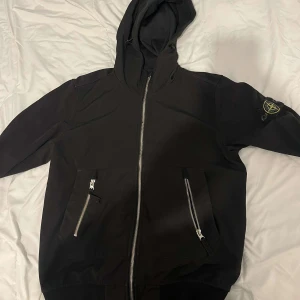 Svart Stone Island Jacka  - Snygg svart stone island jacka och huva. Den har två fickor med dragkedjor framtill och en broderad detalj på ärmen. Perfekt för en casual look. Pris kan diskuteras!