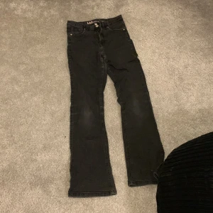 Svarta jeans från LAB Industries - Snygga svarta jeans från LAB Industries i storlek 164. De har en klassisk design med knapp och dragkedja framtill. Perfekta för en stilren look.