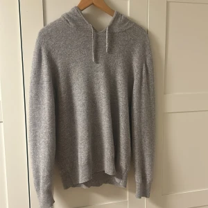 Grå cashmere hoodie - Säljer en mysig grå hoodie med långa ärmar och huva. Perfekt för kyliga dagar och avslappnade stunder. Den har en enkel design som passar till det mesta. Hör av dig vid intresse!