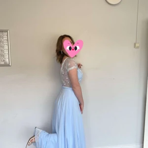 Ljusblå långklänning med spetsdetaljer -  ljusblå balklänning med vacker spets upptill och öppen rygg. Klänningen har en flytande kjol och korta ärmar i spets. Har använt den vid ett tillfälle så väldigt bra skick 🩵