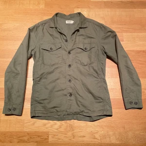 Overshirt från East West - Säljer en stilren grön overshirt från East West. Overshirten är i bra skick och är i storleken M. Overshirten passar perfekt över en hoodie och mycket mer samt perfekt för en trendig stil. Video frågor är det bara att höra av sig💛