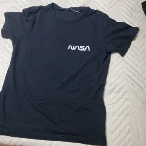 Svart NASA t-shirt - Säljer en svart t-shirt med NASA-logga i vitt på bröstet. T-shirten har en klassisk rund hals och korta ärmar. Perfekt för rymdentusiaster! 🚀
