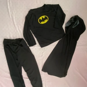  Batman Barn dräkt I 3 Delar  - Säljer en svart Batman-dräkt med den ikoniska gula loggan på bröstet. Dräkten inkluderar en långärmad tröja, byxor och en cape. Perfekt för maskerad eller temafest! Stlk kvar S 2-3 år , M 4-5år och L 6-8 år 165kr/paket , helt ny 