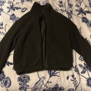 Grön teddyjacka från Jacqueline de Yong - Mysig grön teddyjacka från Jacqueline de Yong i storlek M. Jackan har en dragkedja framtill och är perfekt för kyligare dagar. Den fluffiga texturen ger en trendig look och den är lätt att matcha med olika outfits.