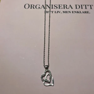 Silverfärgat halsband med hjärthänge från ur&penn  - Elegant silverfärgat halsband med ett dubbelt hjärthänge. Hänget har en glittrig detalj som ger en extra touch av stil. Perfekt för att komplettera din look med en romantisk känsla. Aldrig använd. Köpt från ur & Penn. Säljer för 75 kronor.✨