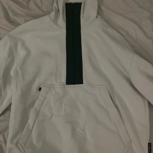 Vit hoodie från Sail Racing - Säljer en stilren vit hoodie från Sail Racing med dragkedja och stor ficka framtill. Perfekt för kyliga dagar med sin bekväma passform och höga krage.