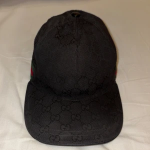 Svart Gucci keps - Svart Gucci keps som använts mycket, defekterna är att lädret gått upp på skärmen och att jag råkade dra av en tråd vid märket på sidan så att det bildades en defekt. Trotts detta så är kepsen väldigt snygg och har en skön passform för ditt huvud. Defekterna syns inte jätte mycket i verkligenheten men ni får skriva för fler bilder👍äkta såklart😁