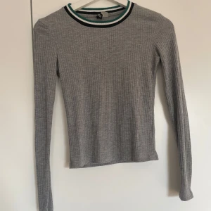 Grå ribbad tröja med randig krage - Säljer en stilren grå ribbad tröja med lång ärm och en randig krage i grönt och svart. Perfekt för en avslappnad look.