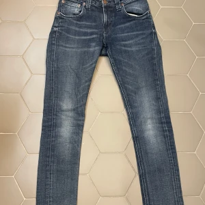 Nudie Jeans - Snygga mörkblå jeans från Nudie Jeans med klassisk femficksdesign och knappgylf. Jeansen har en straight passform och är tillverkade i högkvalitativt denim. Perfekta för en stilren look.