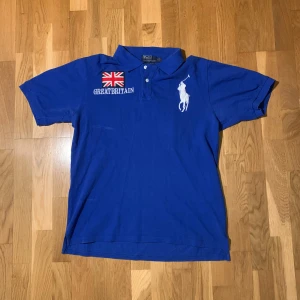 Polo Ralph Lauren piké - Snygg blå ”Chief Keef” pikétröja från Polo Ralph Lauren med broderad logga och texten 'GREAT BRITAIN'. Tröjan har korta ärmar och nummerdetaljer på ärm och rygg. Perfekt nu till våren och sommaren. Var inte rädda att skriva ifall mer frågor eller bilder!