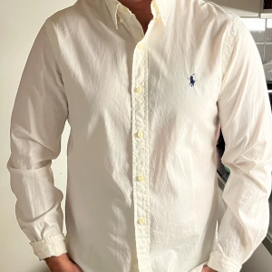 Vit skjorta från Ralph Lauren - Säljer en stilren vit skjorta från Ralph Lauren i slim fit. Skjortan har långa ärmar och är tillverkad i ett lätt twillmaterial. Den har klassiska knappar och en broderad logotyp på bröstet. Storlek M och Skick 9/10 ✅