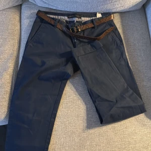 Mörkblå chinos från Zara Man - Snygga mörkblå chinos från Zara Man med ett stilrent bälte. Byxorna har en klassisk design med dragkedja och knappar. Perfekta för en stilren look.