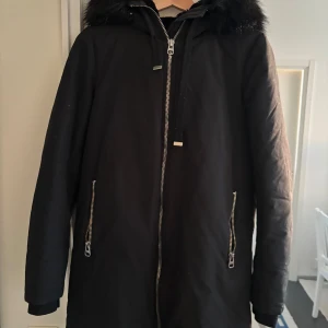 Svart parkajacka från Zara - Snygg svart parkajacka från Zara med dragkedja och fuskpälsdetaljer på huvan. Jackan har långa ärmar och praktiska fickor med dragkedja. Perfekt för kyliga dagar.