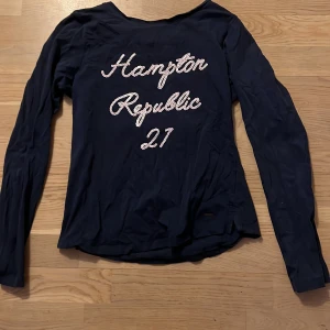 Mörkblå långärmad tröja från Hampton Republic - Snygg mörkblå långärmad tröja från Hampton Republic med texten 'Hampton Republic 27' i glittriga paljetter på framsidan. Perfekt för en avslappnad stil med en touch av glamour.
