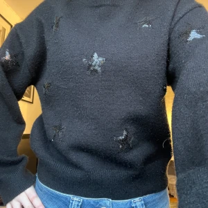 Svart tröja med stjärnor från Ganni - Säljer en svart tröja från Gina Young med glittriga stjärnor. Tröjan har långa ärmar och en normal passform. Perfekt för att lägga till lite stjärnglans i vardagen! 🌟