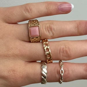 Ringar - Snygga guldfärgade ringar i olika stilar. En ring har en stor rosa sten med fyrkantig form, medan de andra har kedjedetaljer. Perfekt för att ge en elegant touch till din look. 50 kr/st