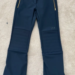Helly Hansen W AVANTI STRETCH PANT - Skidbyxor - Snygga mörkblå  skidbyxor från Helly Hansen med guldfärgade dragkedjor. Byxorna har en quiltad design på benen och är perfekta för kyligare väder. De är både funktionella och stilrena. Jättefint skick. Använda en gång, säljes pga fel storlek. Ord pris 3 300 kr. Färg: NAVY Storlek: XS Bild 2-5 från hemsida.
