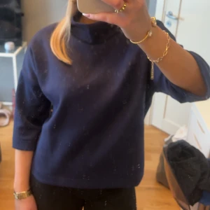 Mörkblå tröja med trekvartsärm - Säljer en stilren mörkblå tröja med trekvartsärm. Tröjan har en hög krage och är tillverkad i ett mjukt material.