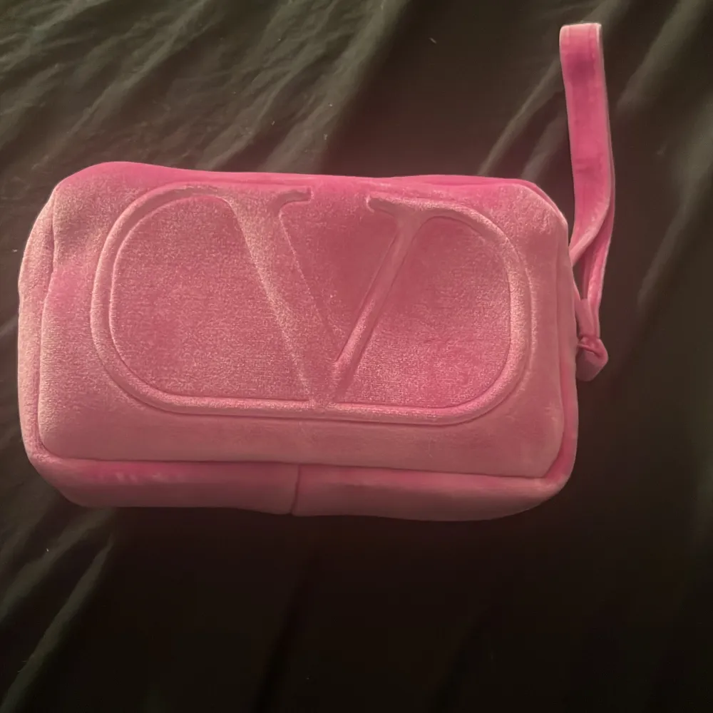 Snygg rosa necessär i sammet med en stor logotyp på framsidan. Den har en praktisk dragkedja och en liten rem för enkel hantering. Perfekt för att förvara smink eller andra småsaker. Använd några få gånger men mest ba legat på sminkbordet . Laukut & Käsilaukut.