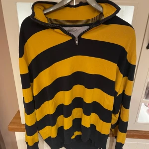 Randig gul och svart tröja med dragkedja - Säljer en cool gul och svart randig tröja med dragkedja vid halsen. Tröjan har långa ärmar och en avslappnad passform, perfekt för en casual look. Tröjan är ifrån dressmann. Storleken är xxl men är mer som en L/XL
