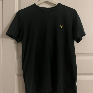 Grön t-shirt från Lyle & Scott - Säljer en stilren grön t-shirt från Lyle & Scott med deras ikoniska gula logga broderad på bröstet. Perfekt för en avslappnad look. Kortärmad och tillverkad i mjukt material.