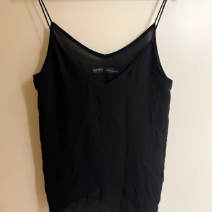 Svart linnetopp från Zara Basic - Snygg svart linnetopp från Zara Basic med tunna axelband och v-ringad hals. Perfekt för en stilren och enkel look. Tillverkad i ett lätt och bekvämt material.