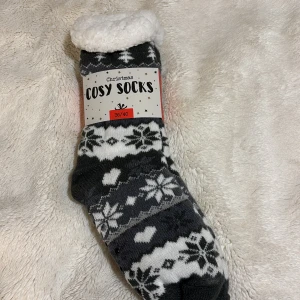 Grå/vita julstrumpor - Tyvärr är julen över men man kan alltid behöva mysiga julstrumpor. Dessa är i grått och vitt med snöflingemönster. Perfekta för kalla vinterdagar med en mjuk insida för extra värme. Eller vem vet? Kanske en vanlig dag där hemma. Stl 36/40.