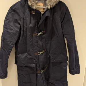 Mörkblå parkajacka från Zara i stl M - Snygg mörkblå parkajacka med pälsdetalj på kragen och spännen framtill. Lite tunnare så passar bra när det inte är -20. Från Zara i stl M.