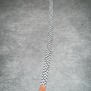 Svartvitt flätat bälte - Snyggt svartvitt flätat bälte med silverfärgat spänne och bruna läderdetaljer. Perfekt för att ge din outfit en stilren touch. Från onewear, nypris -:219kr